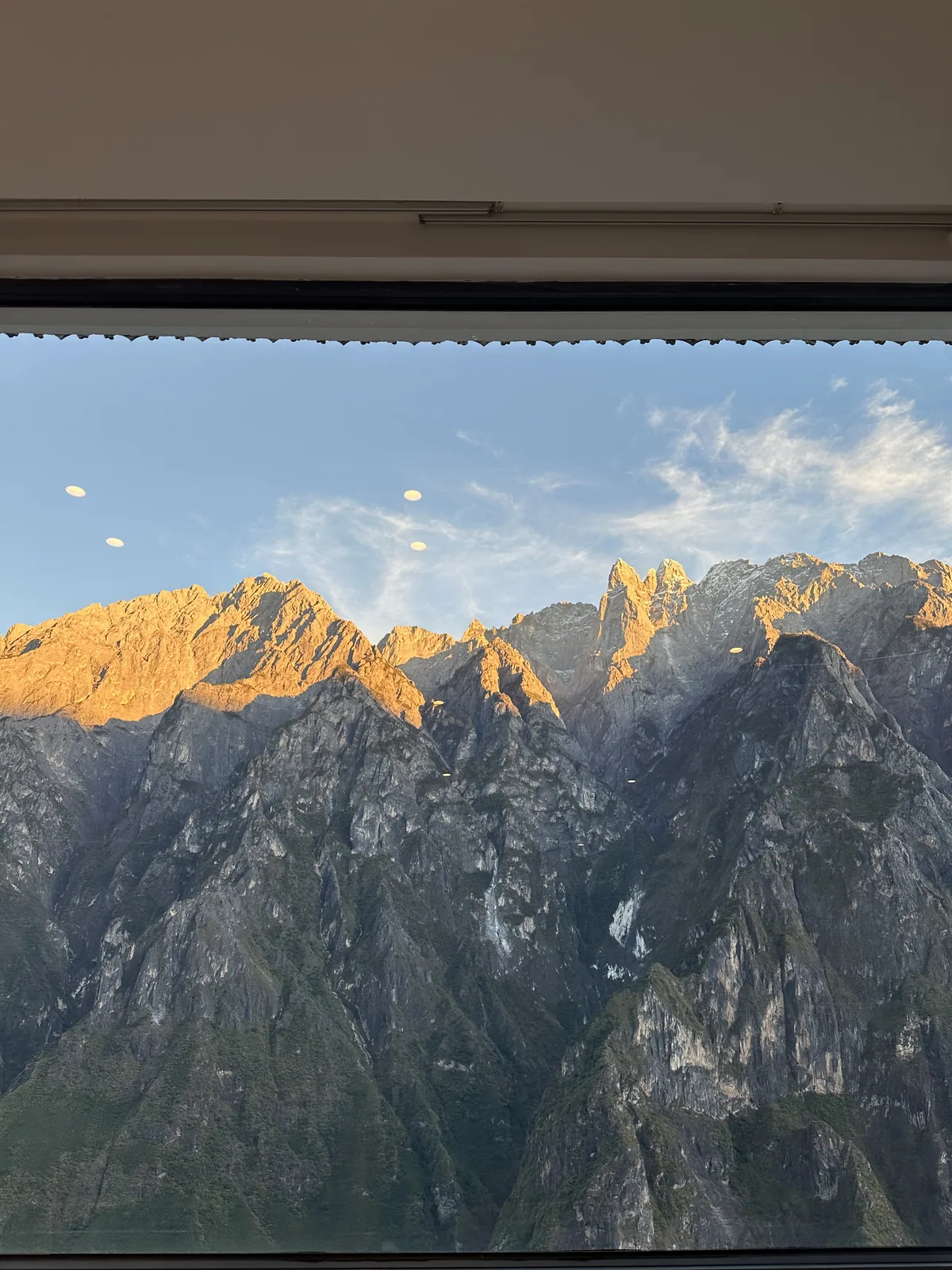 The same guest room window at sunset, with golden light on the snow peaks